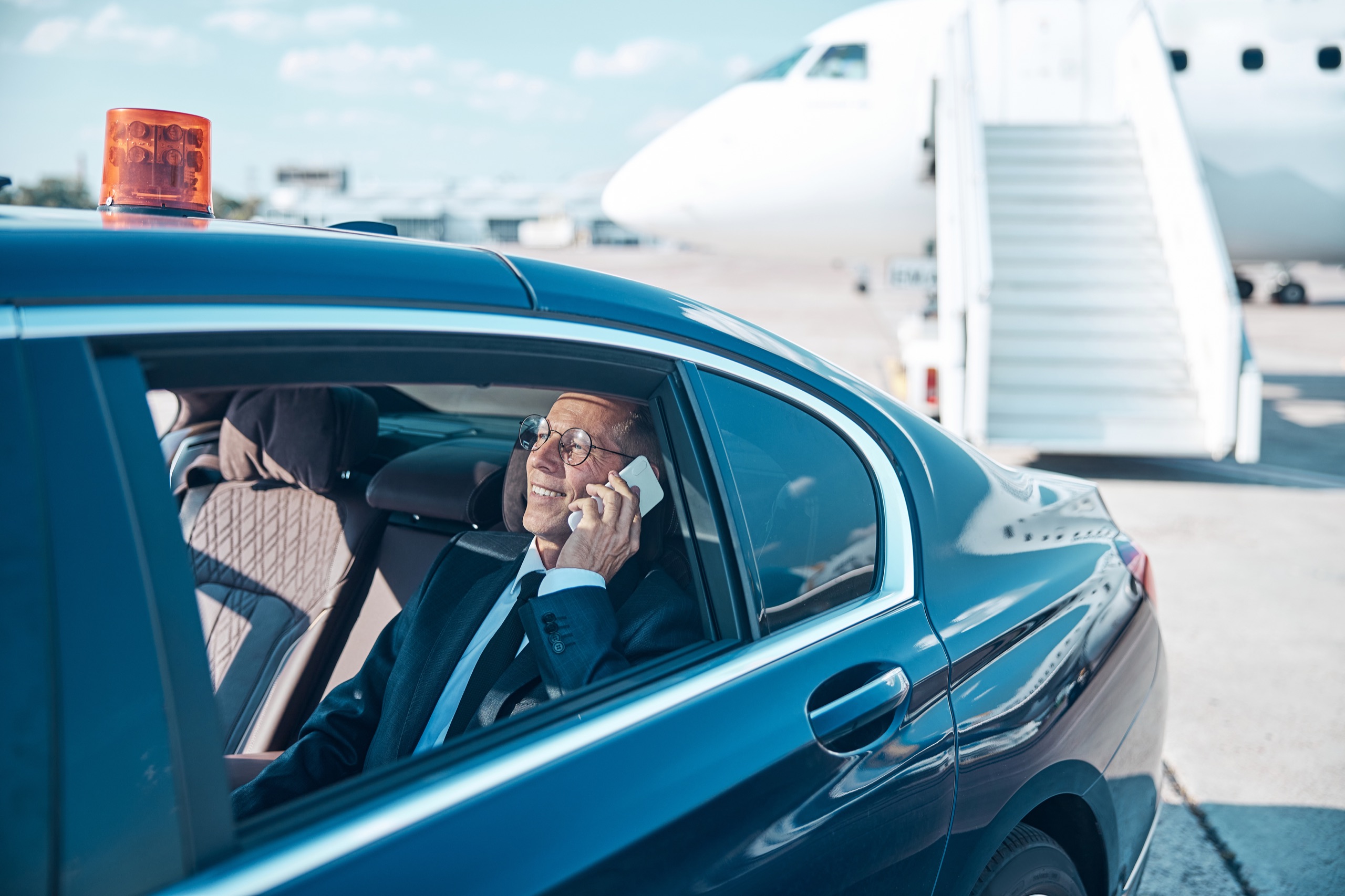 Executive seated in a chauffeured sedan beside an airport aircraft