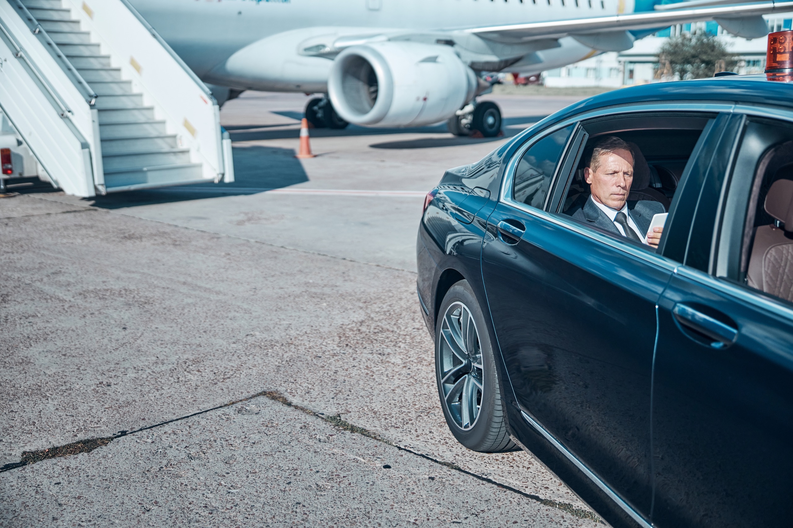 Executive working from a chauffeured car beside an aircraft